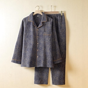 Könnte beinhalten: Ein zweiteiliges Pyjama-Set in einem blau-goldenen geometrischen Muster. Das langärmlige Hemd mit Knöpfen und die passende Hose hängen an einem Holzbügel. Das Hemd hat eine Brusttasche und goldfarbene Verzierungen an Kragen, Manschetten und Tasche.