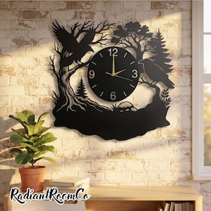 Peut inclure: Une horloge murale noire avec un cadran circulaire, des aiguilles dorées et les chiffres 3, 6, 9 et 12. Elle est entourée d'une silhouette découpée au laser représentant une forêt avec deux corbeaux, l'un en vol et l'autre sur une branche.