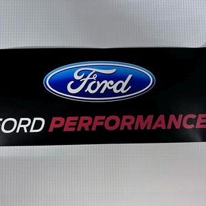 May include: Black rectangular sticker featuring the Ford logo in a blue oval with white text. Below the logo, the words "FORD PERFORMANCE" are printed in white and red.