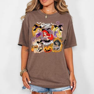 May include: Brown t-shirt featuring a Halloween-themed graphic. The design includes cartoon princesses in witch hats, pumpkins, and the phrases "Spooky Princess Gathering" and "Happy Halloween."