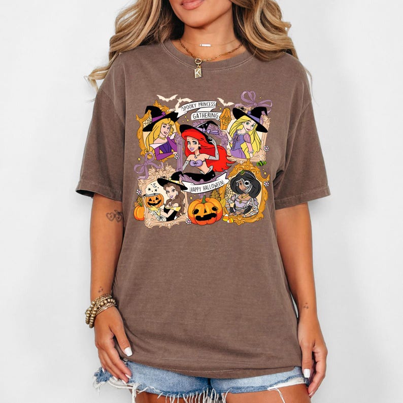 May include: Brown t-shirt featuring a Halloween-themed graphic. The design includes cartoon princesses in witch hats, pumpkins, and the phrases "Spooky Princess Gathering" and "Happy Halloween."