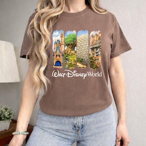Puede incluir: Camiseta marr&oacute;n con un gr&aacute;fico colorido de los monumentos de Walt Disney World, incluyendo un castillo, el &Aacute;rbol de la Vida, Spaceship Earth y el Hollywood Tower Hotel. Las palabras "Walt Disney World" est&aacute;n impresas en blanco debajo.
