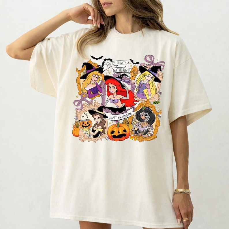 May include: Cream-colored t-shirt featuring a graphic of Disney princesses in Halloween costumes. The design includes the text "Spooky Princess Gathering" and "Happy Halloween", along with pumpkins and bats.