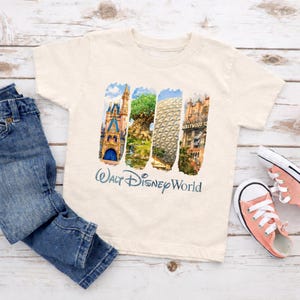 Puede incluir: Una camiseta color crema con un gr&aacute;fico colorido de los monumentos de Walt Disney World. El dise&ntilde;o incluye im&aacute;genes de un castillo, un &aacute;rbol, una esfera geod&eacute;sica y un hotel Hollywood Tower. Las palabras "Walt Disney World" est&aacute;n impresas debajo.