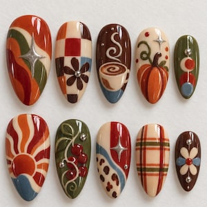 Puede incluir: Un juego de diez uñas postizas en forma de almendra con diseños inspirados en el otoño, que incluyen un sol, patrones de cuadros, una taza de café, una calabaza, bayas, tartán y motivos florales en tonos naranja, verde oliva, marrón y crema.