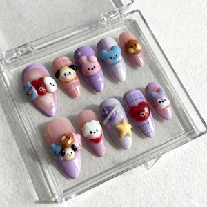 May include: A set of ten artificial nails in a clear plastic case. Each nail is oval-shaped and features a different cartoon character design in various colors, including pink, purple, and blue. Some nails have plaid patterns and star accents.