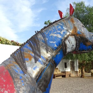 May include: A blue, red, and silver metal sculpture of a horse's head. The sculpture is made of various metal pieces welded together. The horse's mane is made of metal chains.