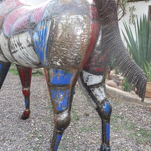 May include: A metal sculpture of a horse, painted in shades of red, white, and blue. The horse's tail is made of metal chains.
