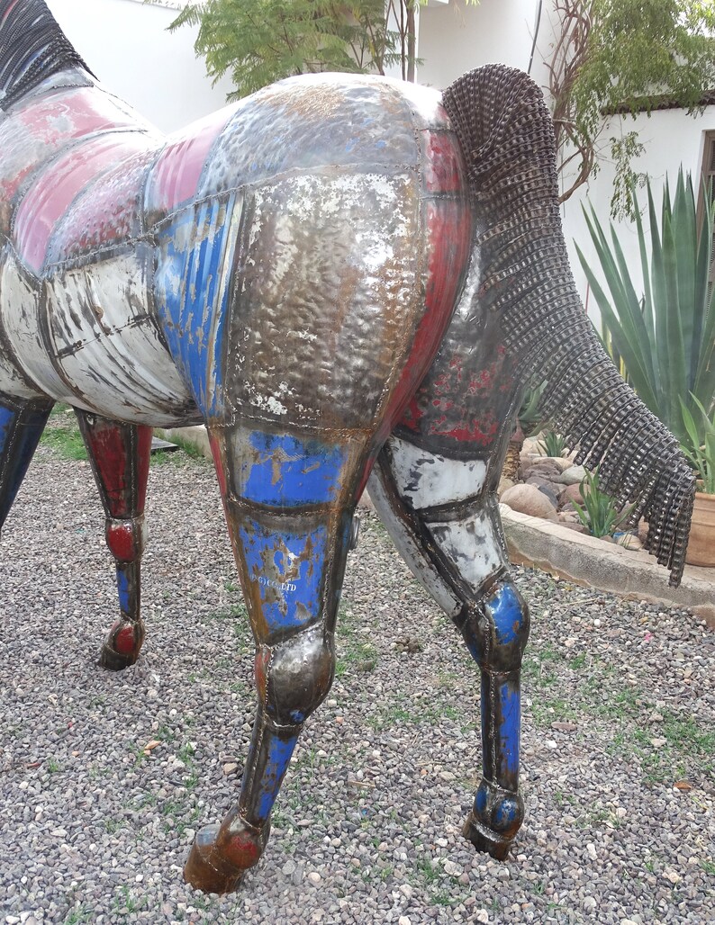 May include: A metal sculpture of a horse, painted in shades of red, white, and blue. The horse's tail is made of metal chains.