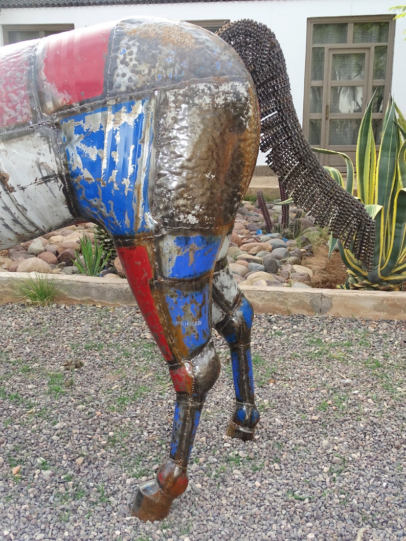 May include: A metal sculpture of a horse with a patchwork design of red, blue, and white. The horse's tail is made of metal chains.