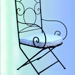 May include: A black metal folding chair with a white cushion. The chair has a decorative, scrolled design.