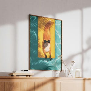 May include: A framed wall art print featuring an illustration of an orange fox wearing black sunglasses, lying on a yellow rectangular pool float in turquoise water, with dark palm leaf shadows cast across the scene in a vertical orientation.