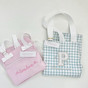 May include: Two pink and blue gingham aprons with white straps. The pink apron has the text "london" embroidered on it. The blue apron has a large white "P" embroidered on it with the text "Phoenix" underneath.