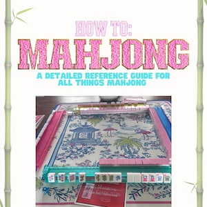 May include: A Mahjong game set featuring pink and white tiles arranged on a patterned mat with a blue and white pagoda and flamingo design. The text reads HOW TO: MAHJONG A DETAILED REFERENCE GUIDE FOR ALL THINGS MAHJONG and includes a 2026 card.