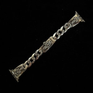 May include: Silver watch strap with a curb chain design. The strap features decorative elements including daggers and ornate emblems. The strap is designed to attach to a smartwatch and has a clasp closure.