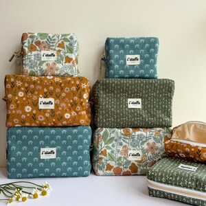 Puede incluir: Una colección de neceseres rectangulares en varias telas estampadas con flores y otros diseños. Las bolsas son en tonos turquesa, amarillo mostaza y verde oliva. Cada bolsa tiene cierre de cremallera y una pequeña etiqueta que dice "l'étoffe".