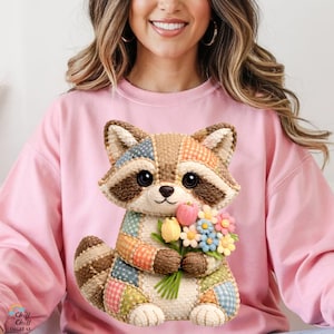 May include: A pink sweatshirt with a patchwork raccoon design holding a bunch of flowers. The raccoon has large eyes and is made from various fabric patches. The sweatshirt has the text "Chill Digital" at the bottom left.