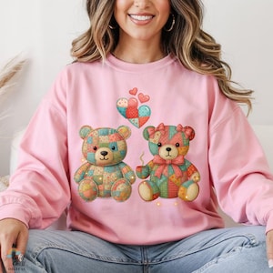 May include: Pale pink sweatshirt with a patchwork teddy bear design. The graphic shows two teddy bears, hearts, and a coffee cup. The bears have bows and are surrounded by small lights. The sweatshirt is a soft pink colour.