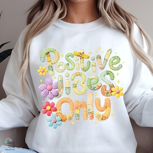Könnte beinhalten: Weißes Sweatshirt mit dem Text "Positive Vibes Only" in einem farbenfrohen, strukturierten Design. Das Design beinhaltet florale Akzente und Sternformen. Das Sweatshirt ist ein lässiger, bequemer Stil.