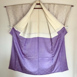 May include: A kimono featuring a two-tone design with a cream-coloured upper section and a vibrant purple lower section. Both sections are decorated with a fine, repeating grid pattern. The garment has wide sleeves and a plain white inner lining.