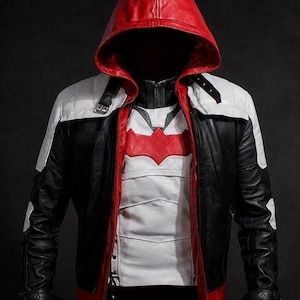 Peut inclure: Une veste à capuche avec une capuche rouge, des manches noires et des empiècements d'épaules blancs. Le devant présente un panneau de poitrine blanc avec un emblème rouge en forme de chauve-souris. Le design inclut des sangles à boucle noires aux épaules et aux poignets, une fermeture éclair frontale et un bord rouge à la base.