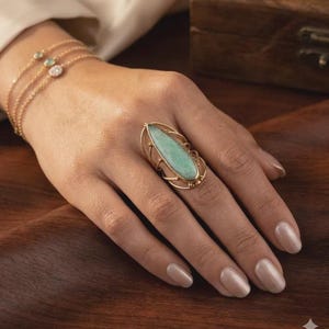May include: A gold ring featuring an oval, pale green gemstone. The ring has an elaborate, openwork design surrounding the stone. A fine gold bracelet with small gemstones is also visible.