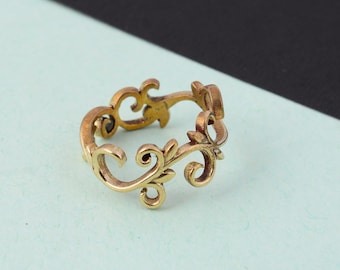 May include: A gold-colored ring with an open design featuring a repeating floral pattern. The ring has a vintage aesthetic and is set against a light blue and black background.