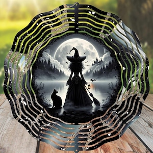May include: A decorative metal wind spinner featuring a witch silhouette with a black cat, broom, and lantern, set against a full moon and forest scene. The outer edge has black and gold wavy stripes. The background is a blurred green.