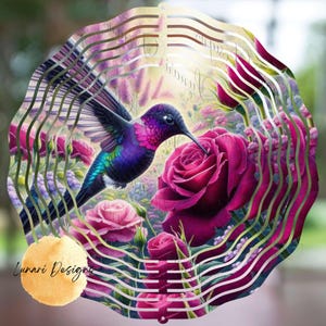 May include: A decorative metal hummingbird wind spinner featuring a vibrant hummingbird with purple, blue, and green feathers, hovering near a large pink rose. The design includes a floral garden scene and the text "Lunari Designs".