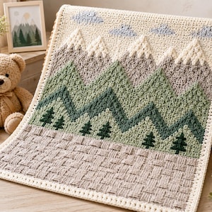 Puede incluir: Una manta rectangular de ganchillo con un diseño de paisaje montañoso en hilo color crema, verde salvia, verde oscuro y gris. El patrón incluye picos nevados, pinos y nubes, con una textura de tejido entrelazado en el borde inferior.
