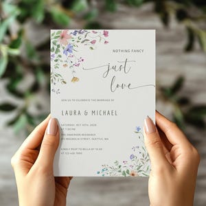 May include: A wedding invitation with floral watercolour accents. The text reads "Nothing Fancy, just love" above the names Laura & Michael. The invitation includes the wedding date, time, and location.