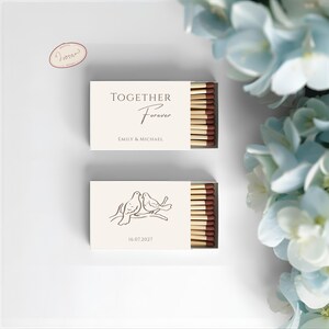May include: Two matchboxes with a wedding theme. The top box reads "TOGETHER Forever" with the names "Emily & Michael." The bottom box features two doves on a branch and the date "16.07.2027."