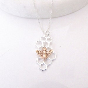 May include: A silver chain necklace with a pendant featuring a gold bee on a silver honeycomb design.