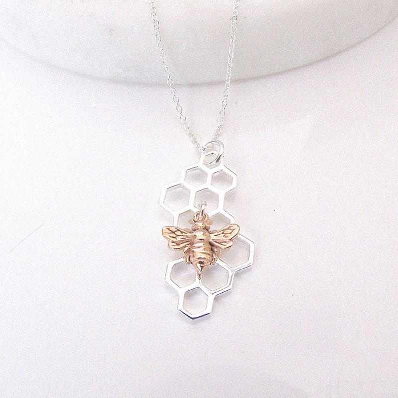 May include: A silver chain necklace with a pendant featuring a gold bee on a silver honeycomb design.