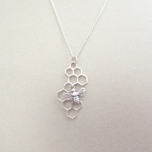 May include: A silver necklace with a bee charm hanging from a honeycomb pendant.