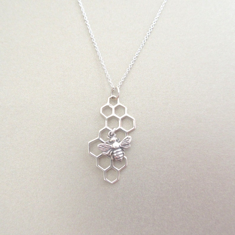 May include: A silver necklace with a bee charm hanging from a honeycomb pendant.