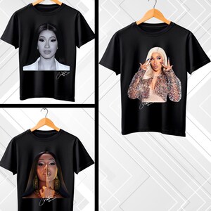 May include: Black t-shirts featuring portraits of a celebrity. Each shirt displays a different image of the celebrity, with a signature. The shirts are hanging on wooden hangers against a white and gray background.