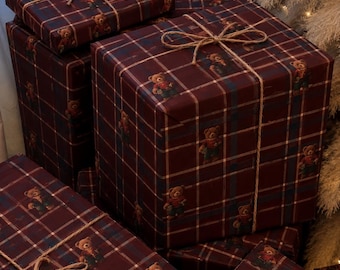 May include: Several square and rectangular gift boxes wrapped in dark maroon plaid paper featuring a repeating pattern of small teddy bears. Each package is tied with thin, natural-colored jute twine arranged in a simple bow on top.