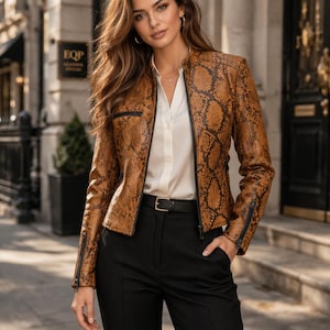 Może przedstawiać: Brązowa skórzana kurtka ze wzorem skóry węża, czarnymi zamkami i czarnym paskiem. Kurtka jest noszona na białej koszuli z kołnierzykiem i czarnych spodniach. Kurtka ma stójkę.