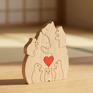 May include: A light-coloured wooden puzzle shaped like a mountain, featuring engraved outlines of five bears of varying sizes. A small, bright red heart is positioned in the centre of the wooden bear family, which is composed of interlocking pieces.