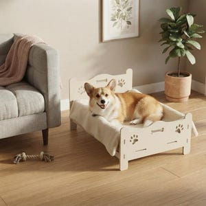 May include: A light-colored wooden pet bed featuring cut-out paw print and bone designs on the headboard and footboard. A tan and white Corgi dog is lying on a soft, cream-colored blanket placed inside the bed frame on a wooden floor.