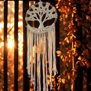 May include: A handmade dreamcatcher featuring a tree motif. The circular frame is crafted from natural wood, with a woven web and a tree silhouette at the centre. Long, white cotton strands dangle from the bottom, creating a bohemian style.