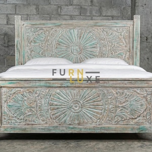 Puede incluir: Un marco de cama de madera tallada y envejecida, con cabecero y piecero. El marco presenta intrincados patrones florales y geométricos con un acabado descolorido en color turquesa y blanco. La cama es de madera y tiene un colchón y almohadas blancos.