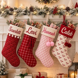 May include: Four quilted Christmas stockings hanging in a row. The first is red with white pom-poms and the name Scarlett. The second is red plaid with tassels and the name Levi. The third is pink plaid with pom-poms and the name Hannah. The fourth is white with red bows and the name Caleb.