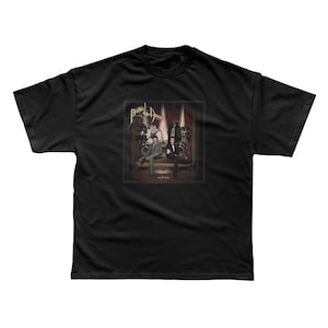 May include: Black t-shirt featuring a graphic of a band posing on a stage. The band's name, "Panic! at the Disco", is printed in gold script above the image. The image includes the text "A Fever You Can't Sweat Out".
