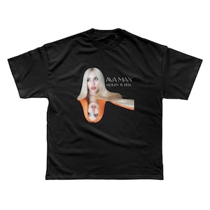 Op de afbeelding: Zwart T-shirt met een afbeelding van Ava Max en haar reflectie. De tekst "AVA MAX" en "HEAVEN & HELL" zijn in het wit gedrukt. De afbeelding toont een vrouw met lang blond haar en rode lippenstift.