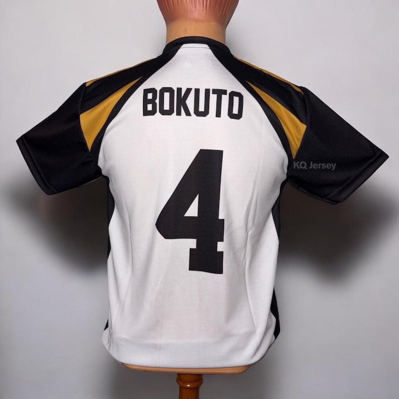 May include: A white and black jersey with gold accents. The name "BOKUTO" is printed across the upper back, with the number "4" below. The jersey has black sleeves and the text "KQ Jersey" is visible.