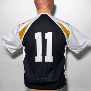 May include: A black and white jersey with the number 11 in white on the back. The jersey has gold accents on the shoulders and the text "KQ Jersey" at the bottom. The jersey is displayed on a mannequin.