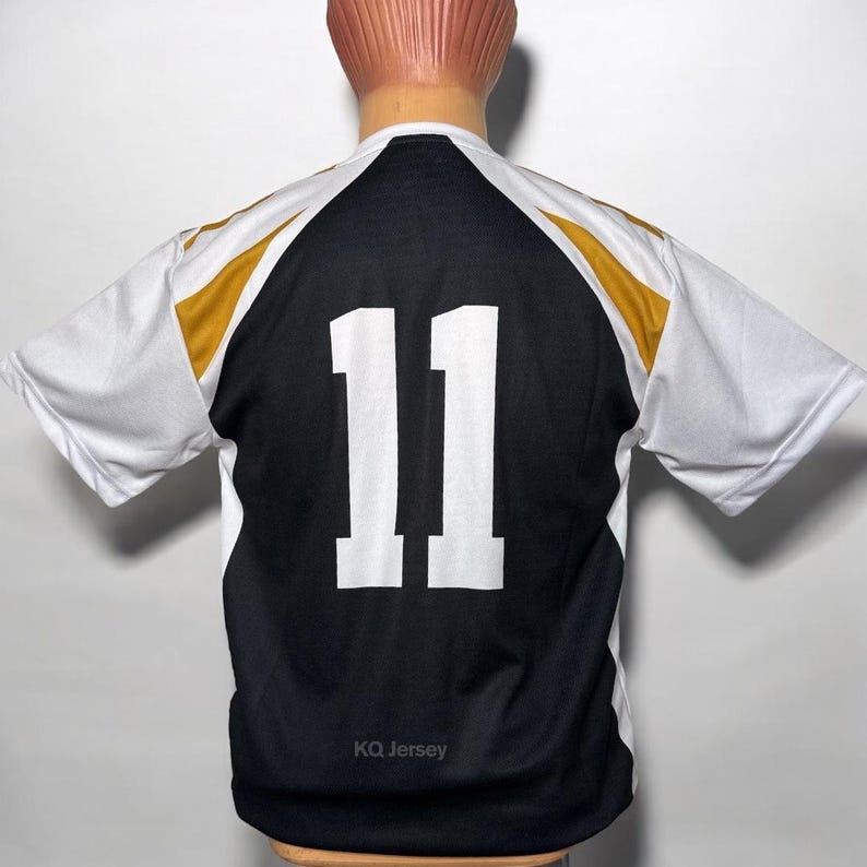 May include: A black and white jersey with the number 11 in white on the back. The jersey has gold accents on the shoulders and the text "KQ Jersey" at the bottom. The jersey is displayed on a mannequin.