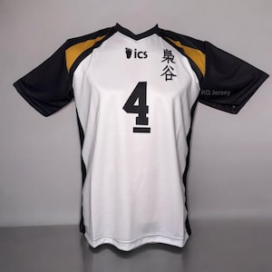 May include: White and black volleyball jersey with the number 4 in black on the front. The jersey has black sleeves and gold accents on the shoulders. The text "ics" and Japanese characters are printed on the front. The text "KQ Jersey" is printed on the sleeve.